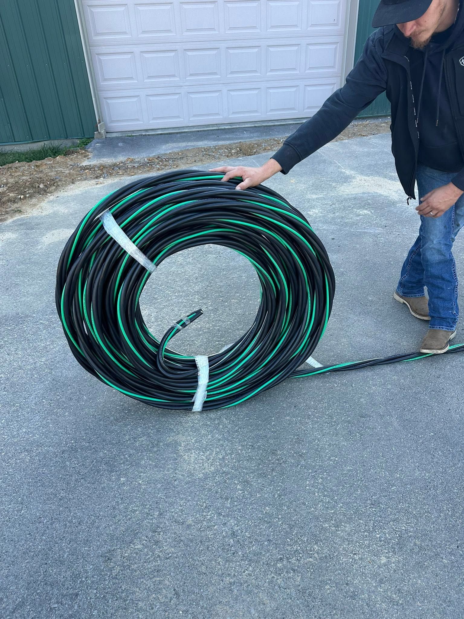 Person rolling a coiled black-and-green hose on a driveway near a garage door