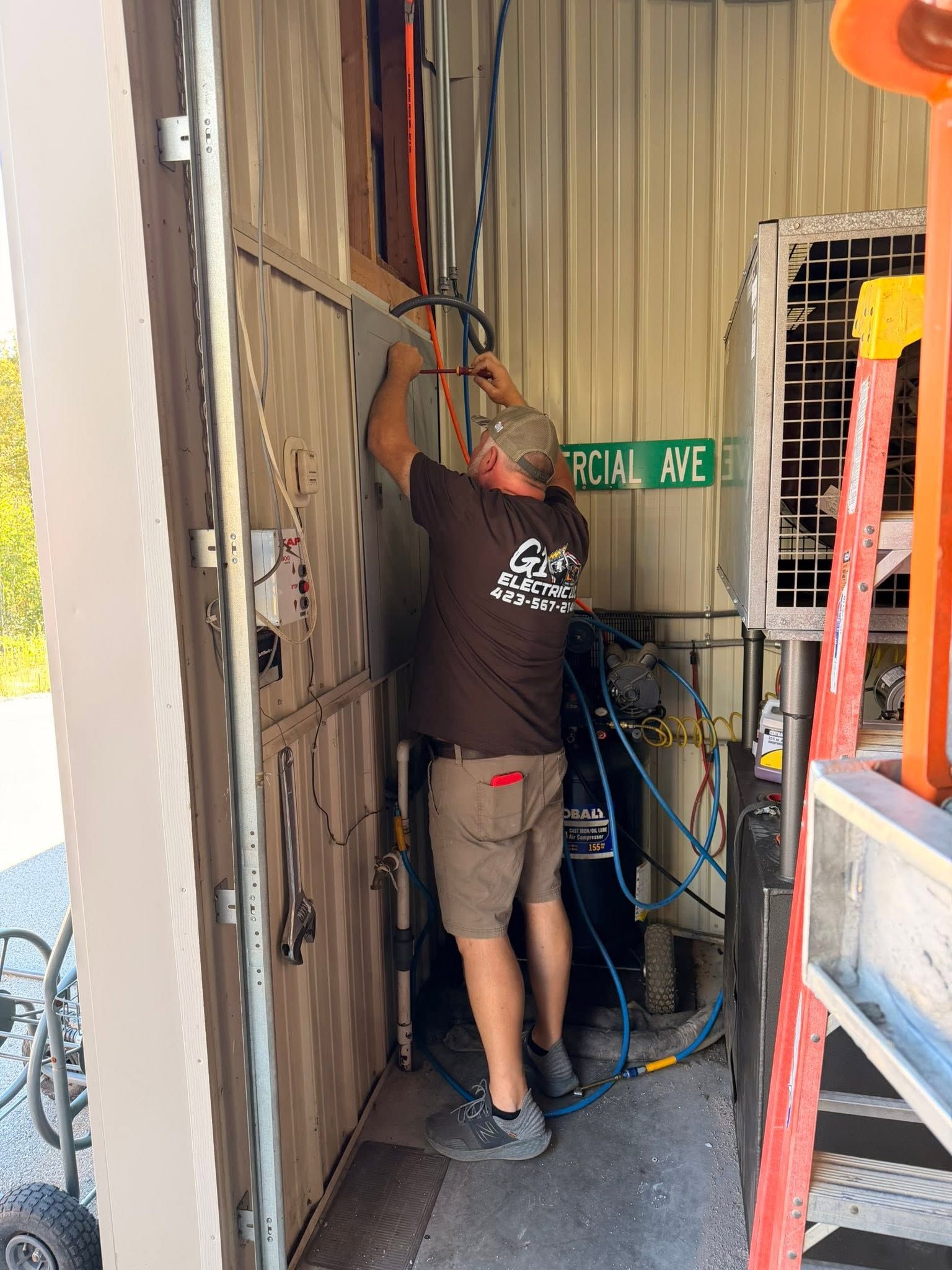 Worker adjusting cables in a narrow utility corridor beside a green EXIT sign and metal shelving.