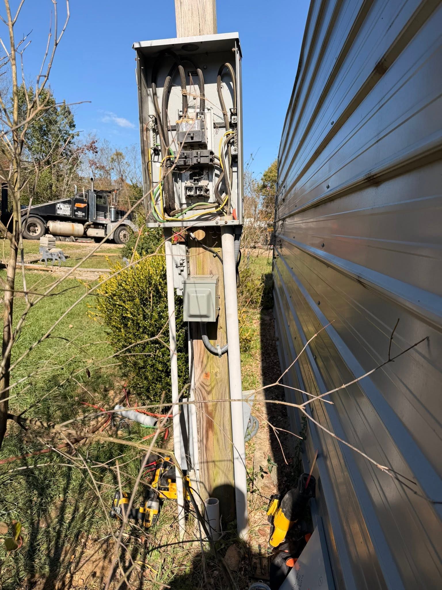 Open electrical meter and utility box on a wooden pole beside a metal-sided building.