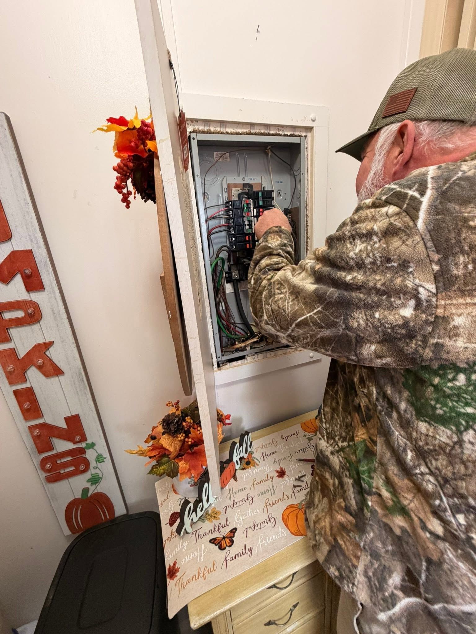 Person in camo jacket working inside an electrical panel on a decorated wall