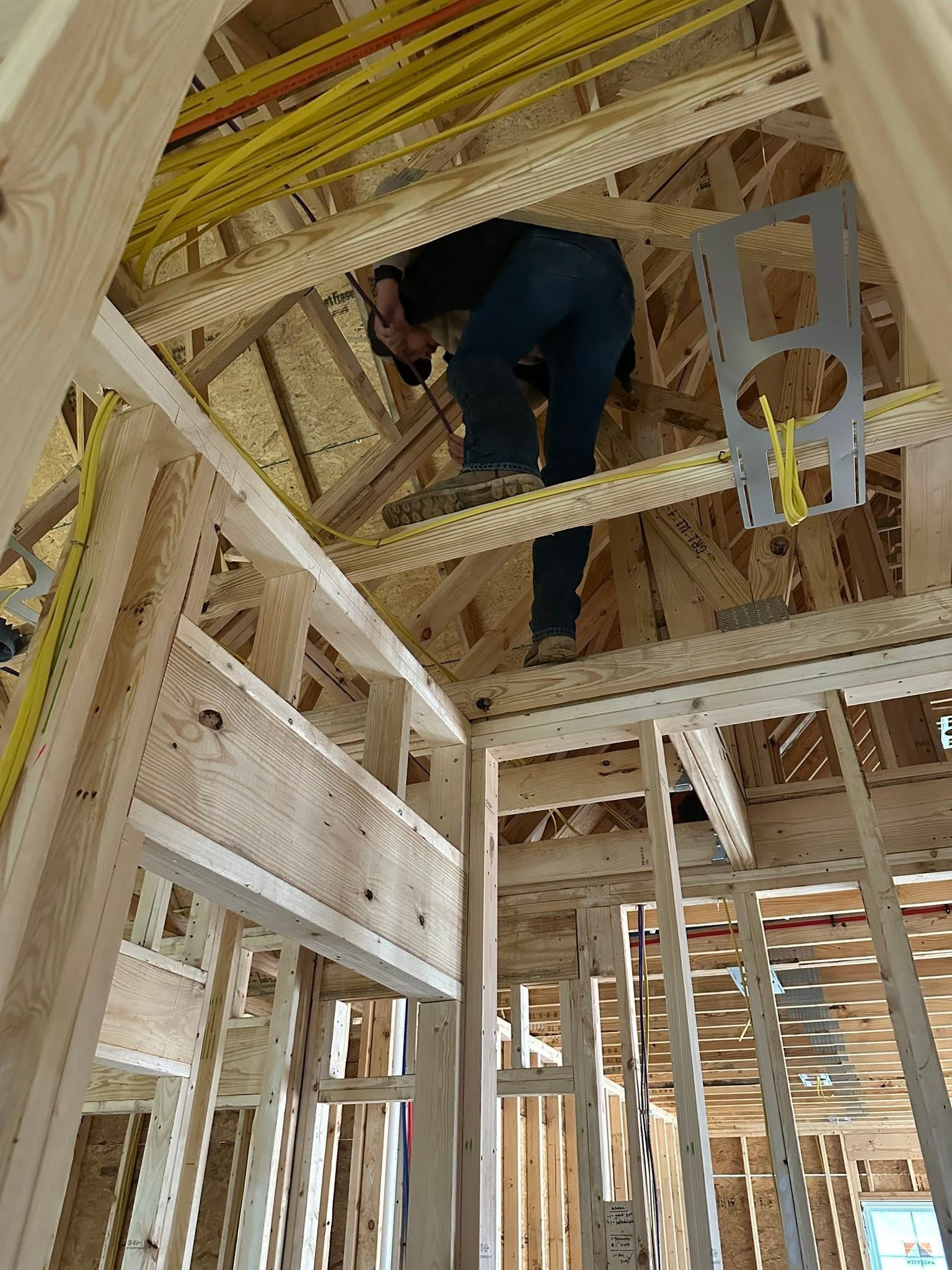 Worker in a framed house, crouching on exposed rafters during construction.