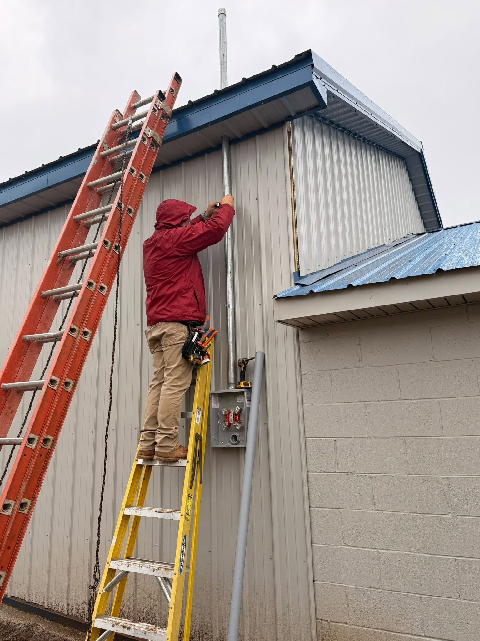 Worker on ladders repairing the roof edge of a metal-sided building
