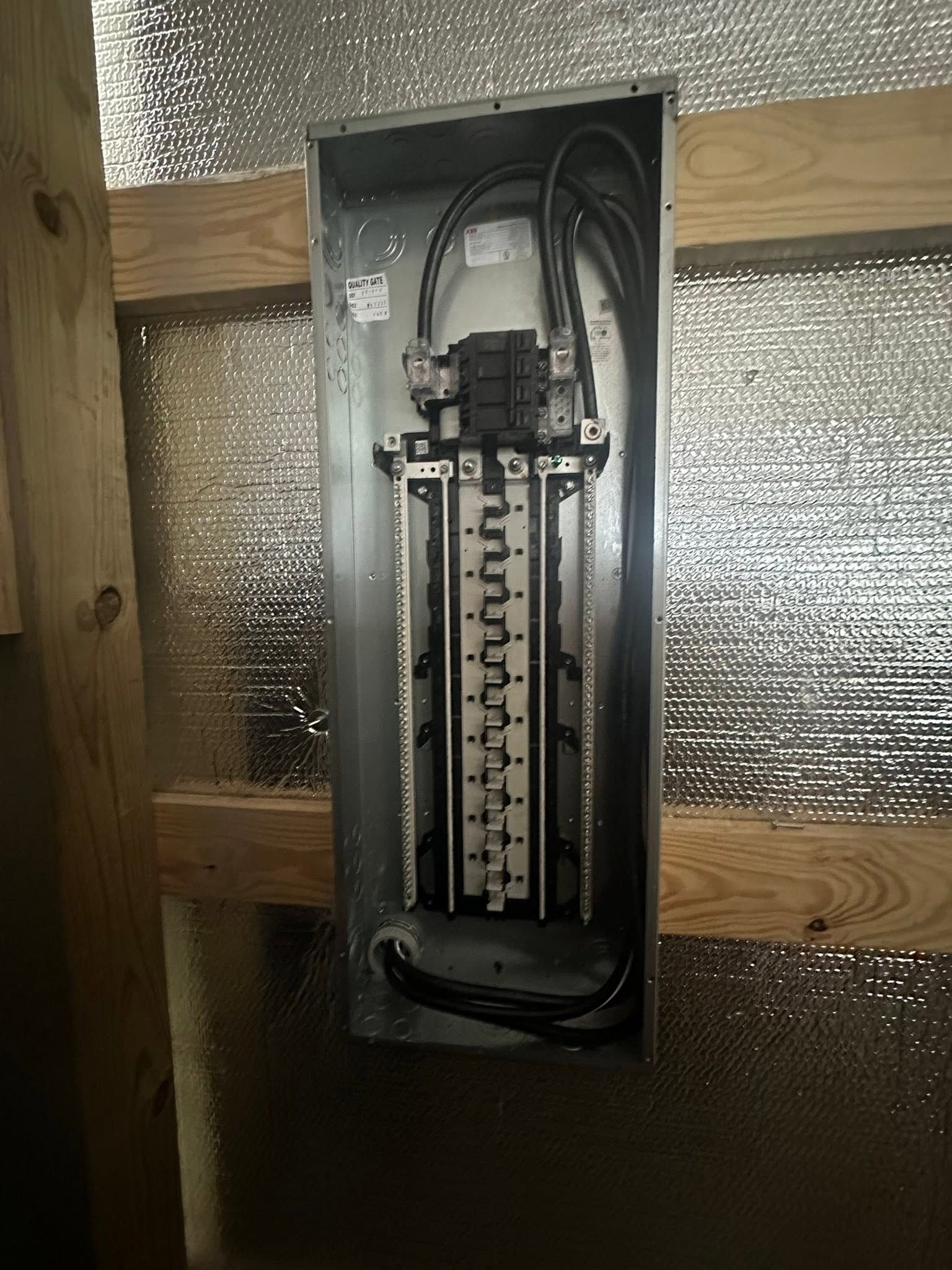 Open electrical breaker panel mounted on a wooden wall with exposed wiring.