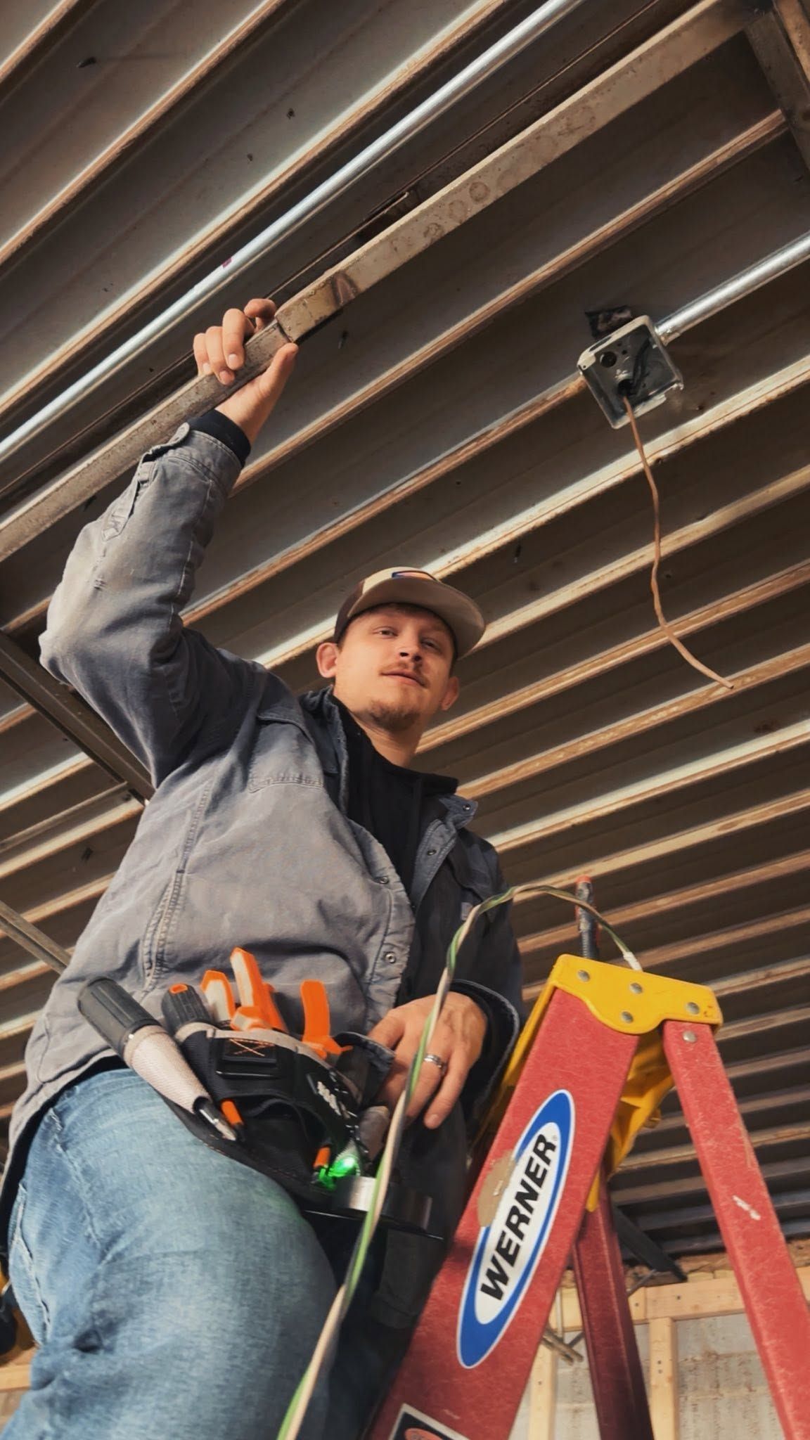 Worker on a red ladder inspecting ceiling beams in an indoor construction site
