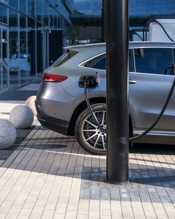 Silver car parked beside a black pole on a paved sidewalk outside a modern glass building.