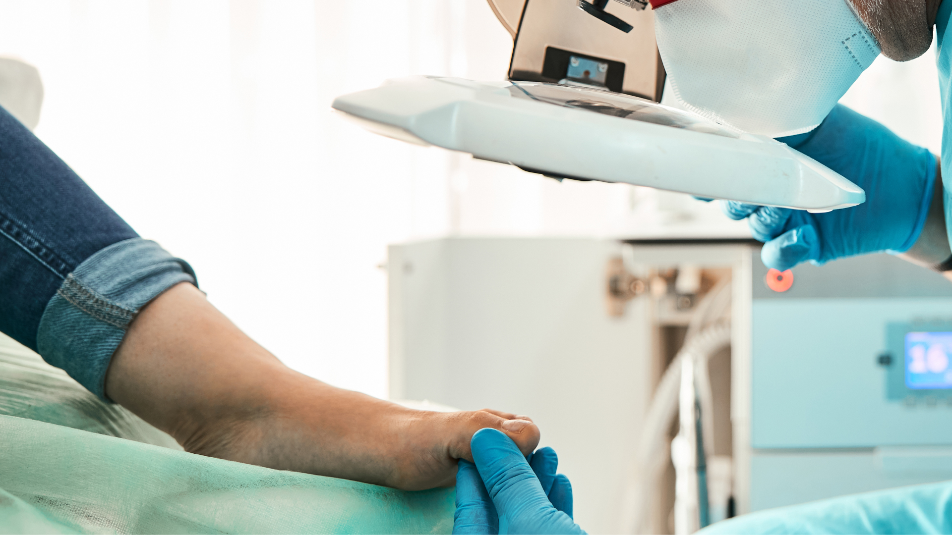 Person receiving foot treatment with a laser device. Doctor wearing blue gloves, focusing the device on the foot.