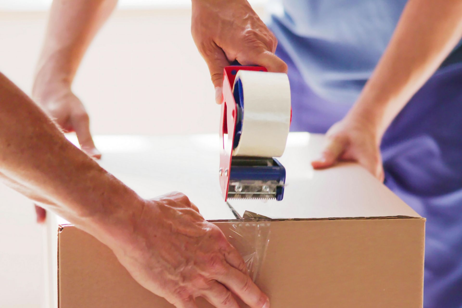 Hands use a handheld tape dispenser to seal a cardboard box.