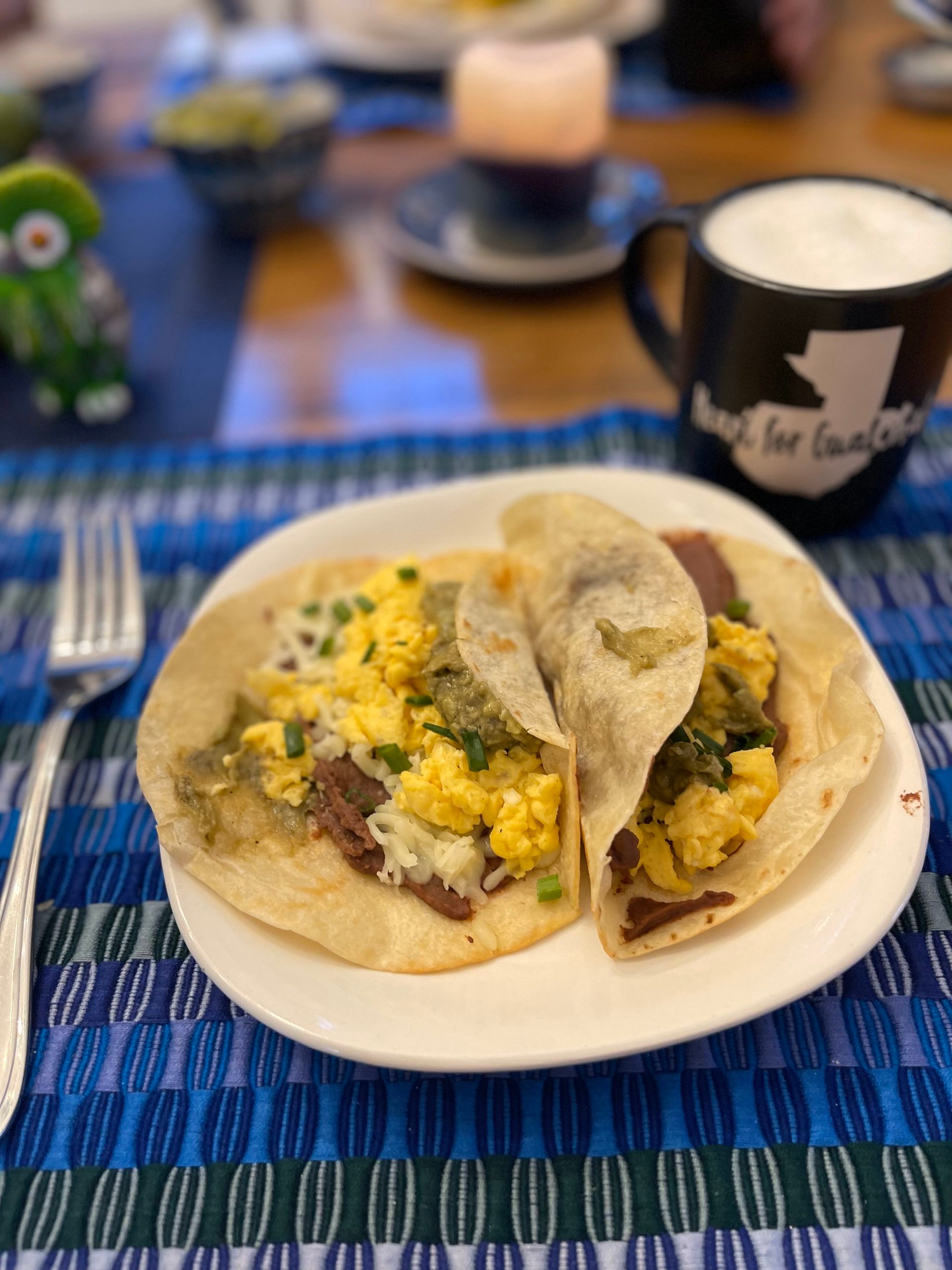 A white plate topped with two tacos and a cup of coffee on a table.