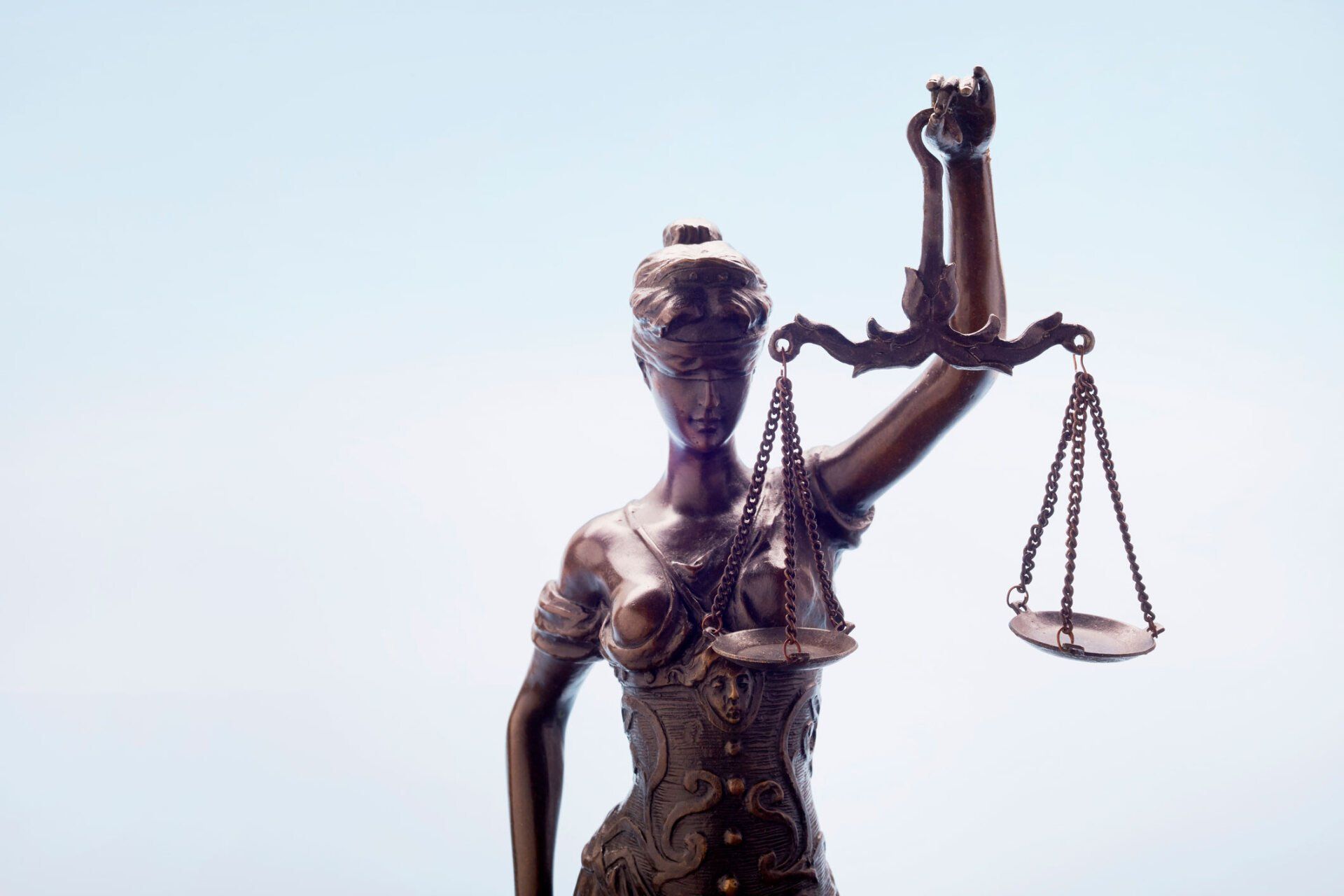 Statue of Lady Justice holding scales, against a light blue backdrop. Statue of Lady Justice holding scales, against a light blue backdrop.