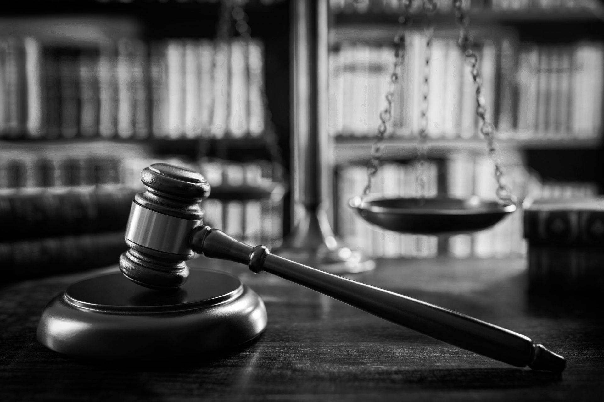 Gavel on a wooden block, scales of justice in background, in front of a bookcase. Gavel on a wooden block, scales of justice in background, in front of a bookcase.