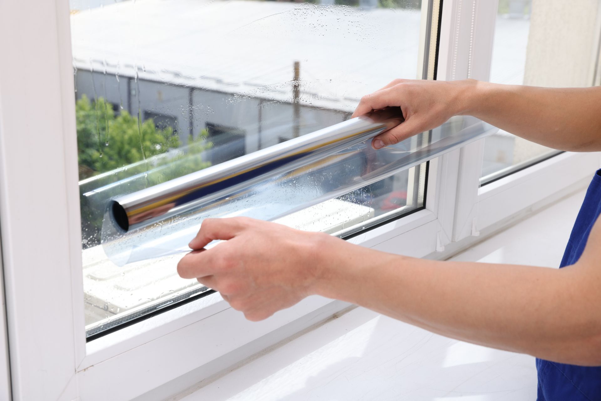 Hands applying clear film to a window with a squeegee