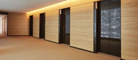 Hallway with wood-paneled walls, elevator doors, and carpeted floor. The lights are on.