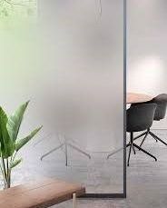 Frosted glass partition reveals a meeting space with a round table and black chairs.