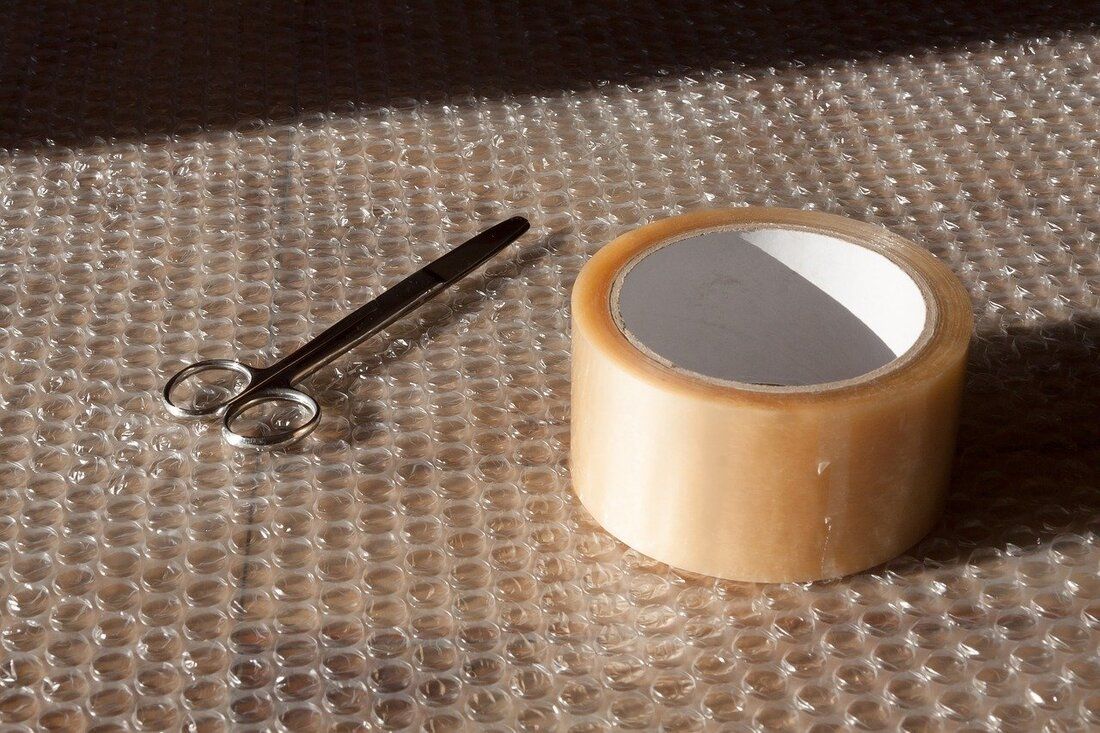Scissors and tape roll on bubble wrap, angled sunlight.
