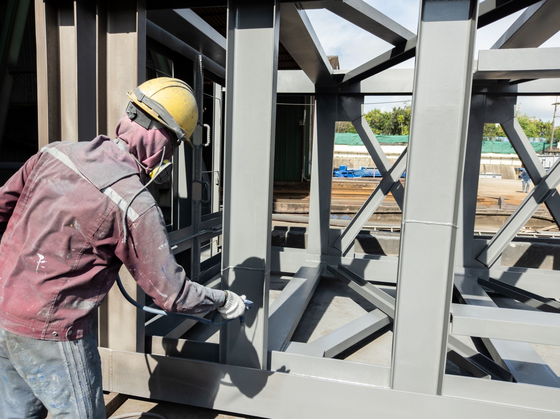 Construction Worker Spraying Grey Paint on A Metal — Phoenix Protective & Marine Coating Specialists in Woree, QLD