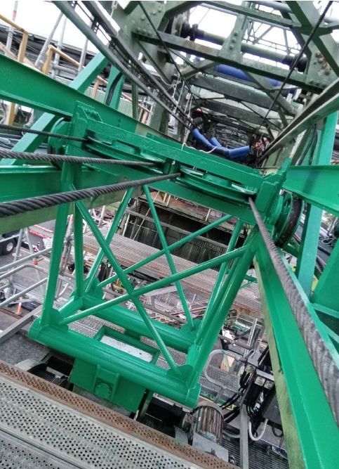 Green industrial crane structure viewed from below inside an indoor metal framework.