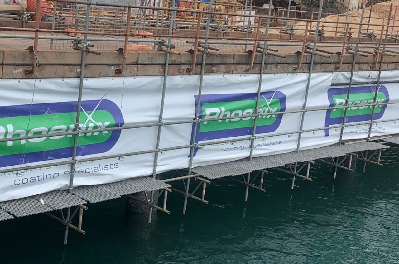 Scaffolding With Phoenix Logo Banner Over Water — Phoenix Protective & Marine Coating Specialists in Woree, QLD