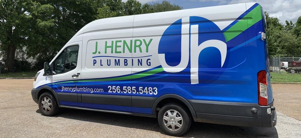 A j. henry plumbing van is parked in a gravel lot.