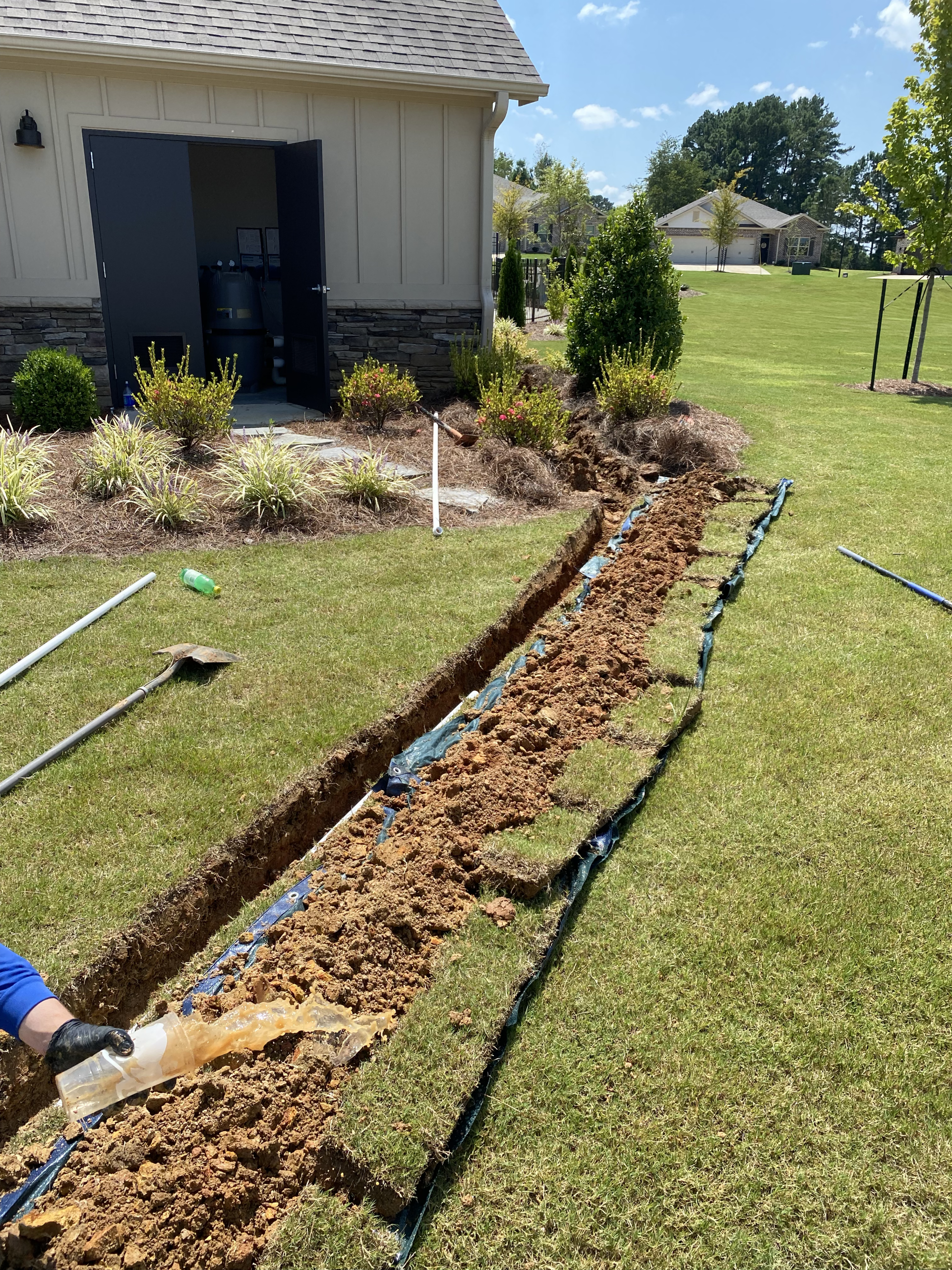 A person is digging a trench in the grass in front of a house.