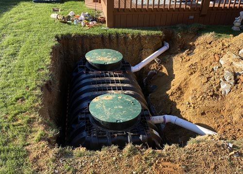 A septic tank is being installed in a hole in the ground in front of a house.