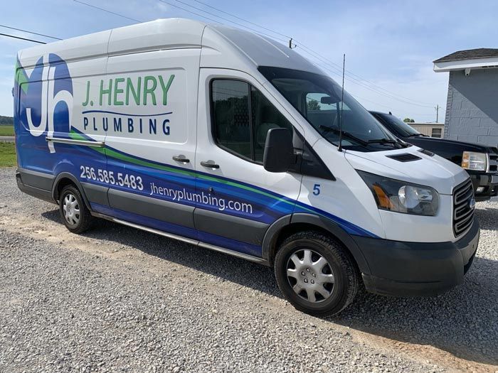 A j. henry plumbing van is parked in a gravel lot.