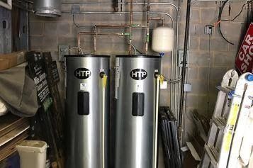 Two water heaters are sitting next to each other in a garage.