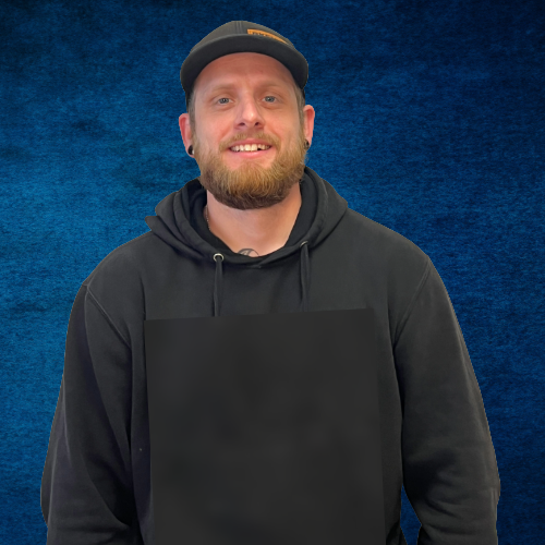 A young man wearing a hat and a blue shirt is standing in front of a blue background.