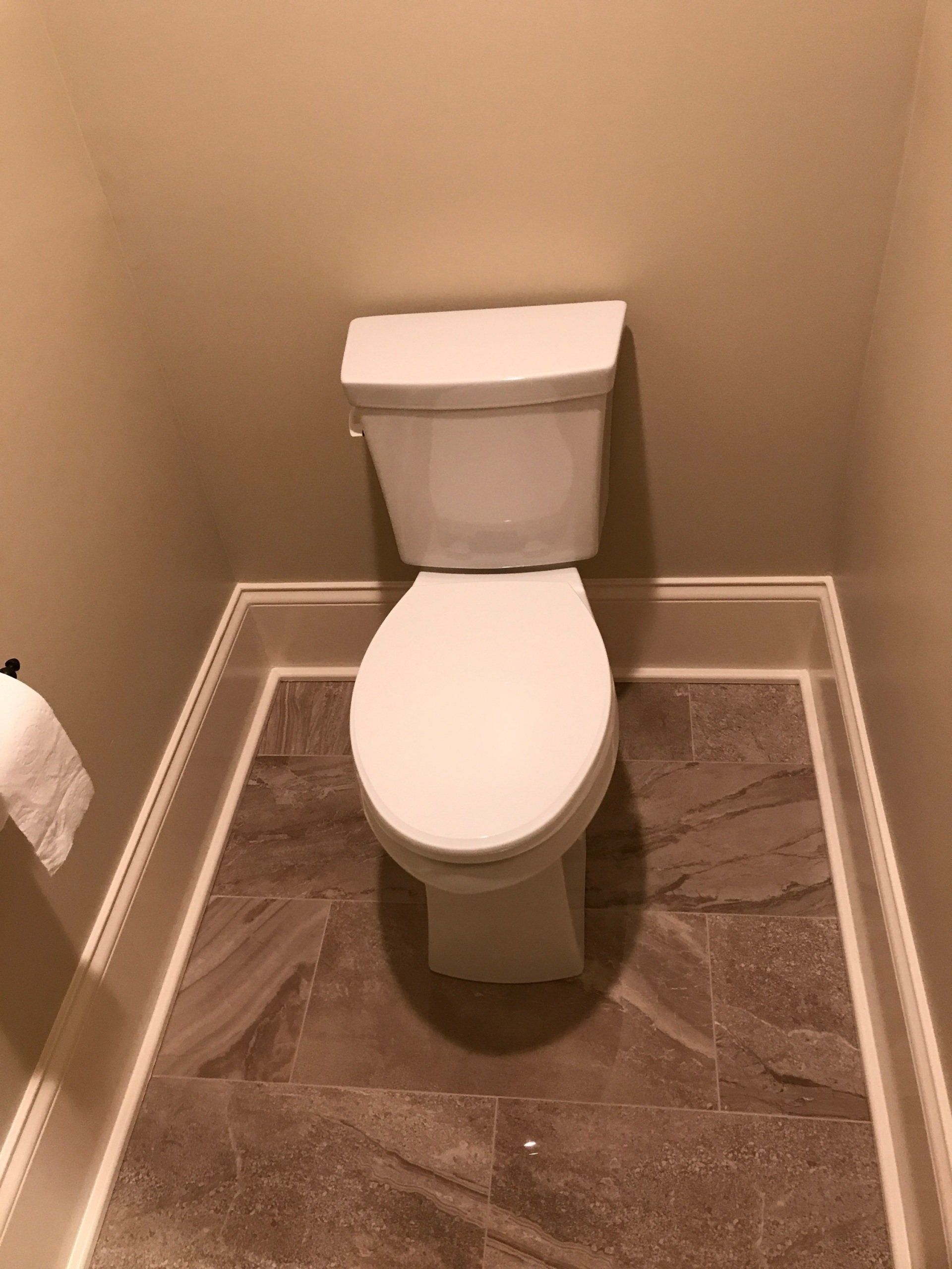 A toilet is sitting on a tiled floor in a bathroom.