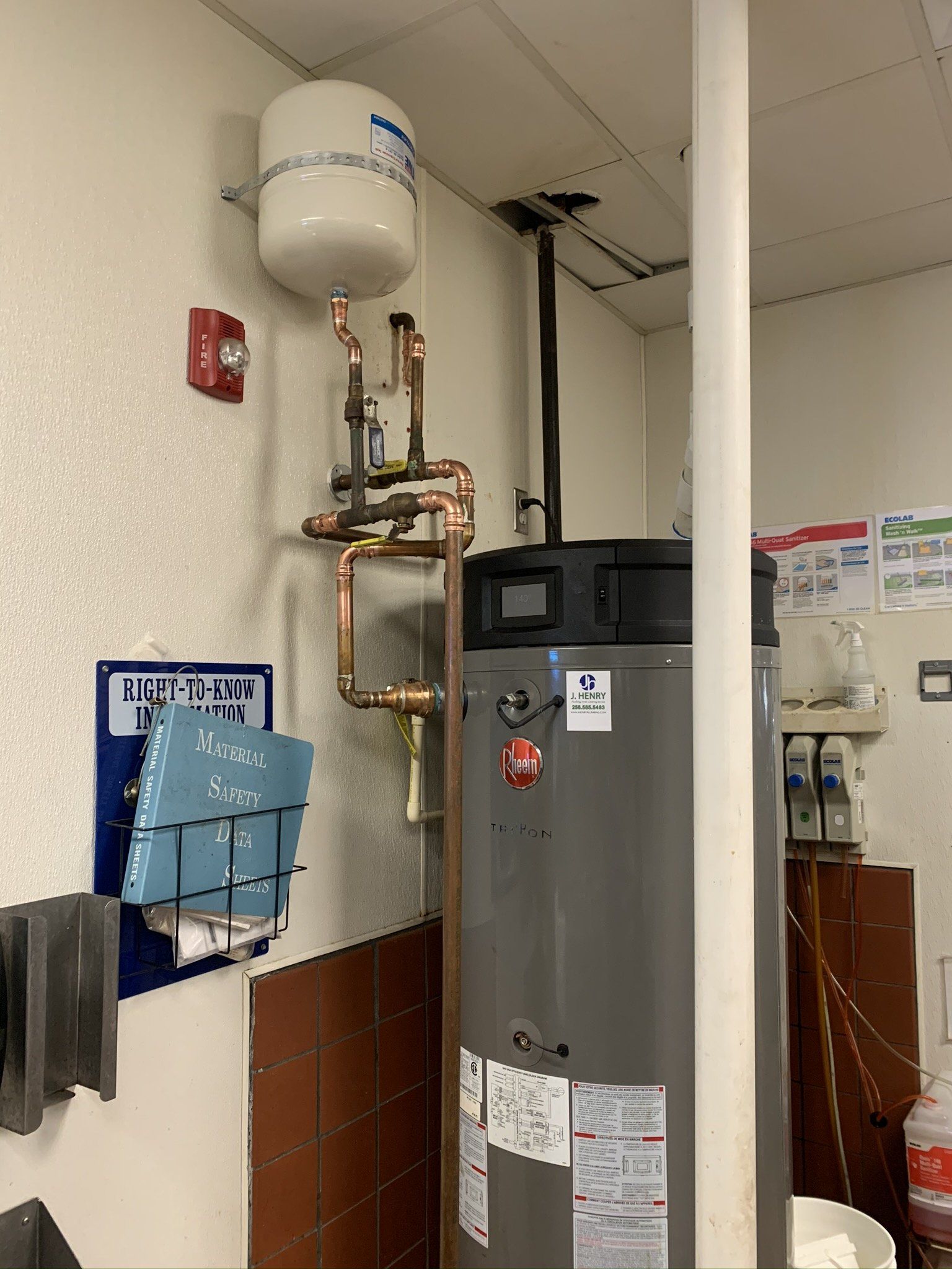 A room with a water heater and a fire alarm on the wall.