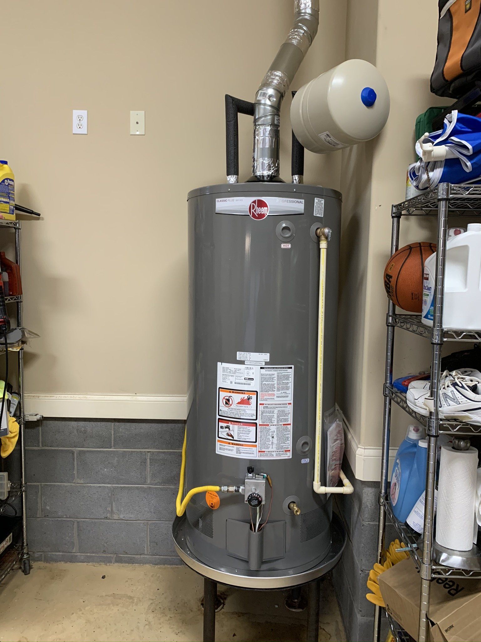 A water heater is sitting in a garage next to a basketball hoop.
