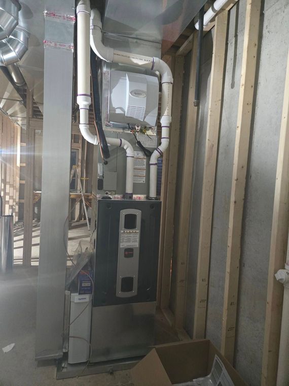 Exposed pipes and HVAC equipment in an unfinished interior wall cavity with insulation and a floor box.
