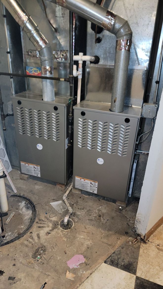 Two gray furnaces with metal ducts in a utility closet