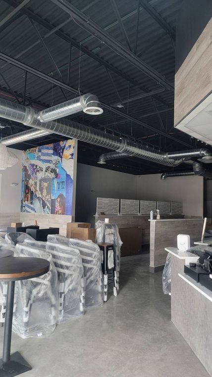 Empty industrial-style café interior with stacked chairs, tables, and exposed ceiling ducts