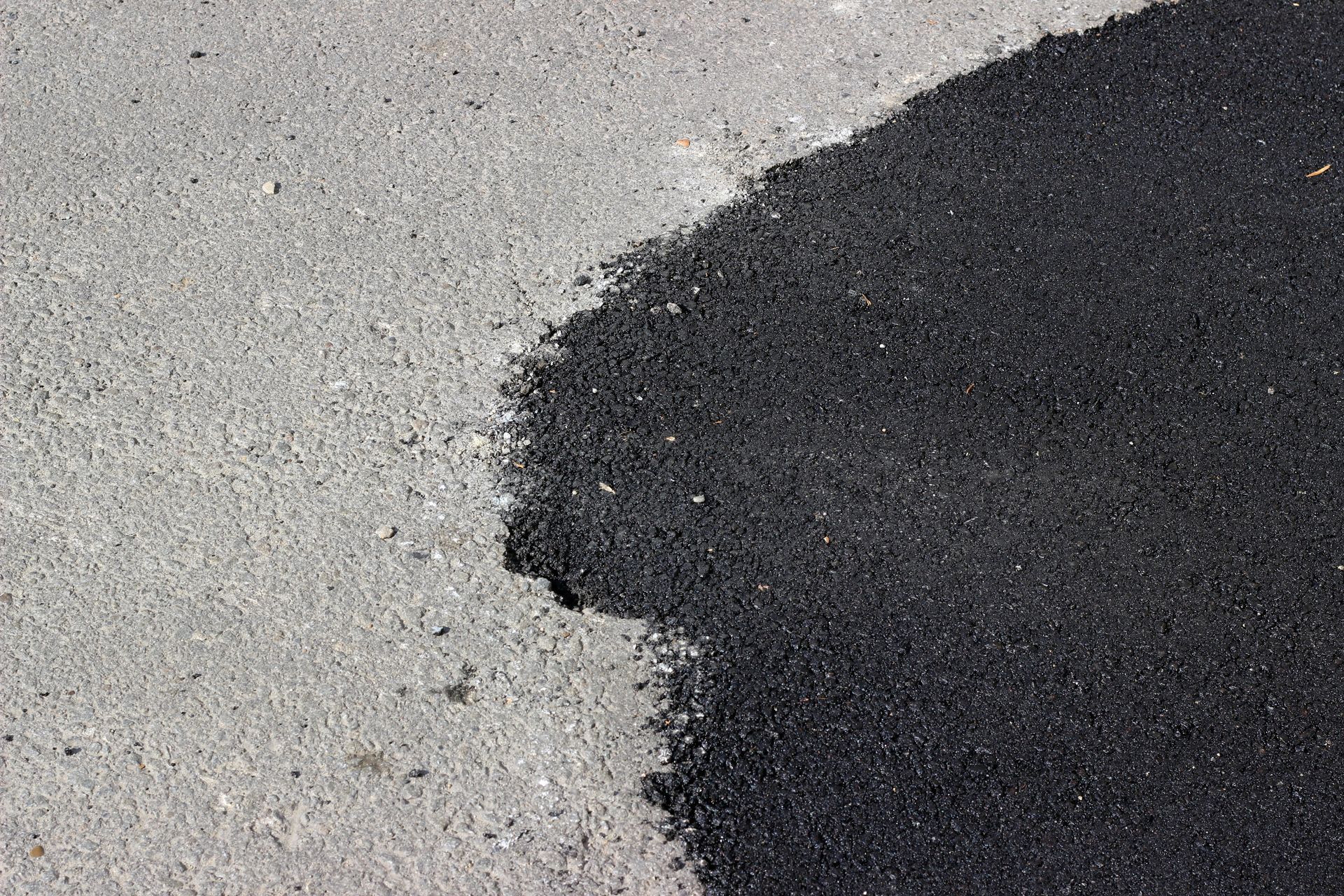 Fresh asphalt patch applied to a worn concrete or paved road surface. Fresh asphalt patch applied to a worn concrete or paved road surface.