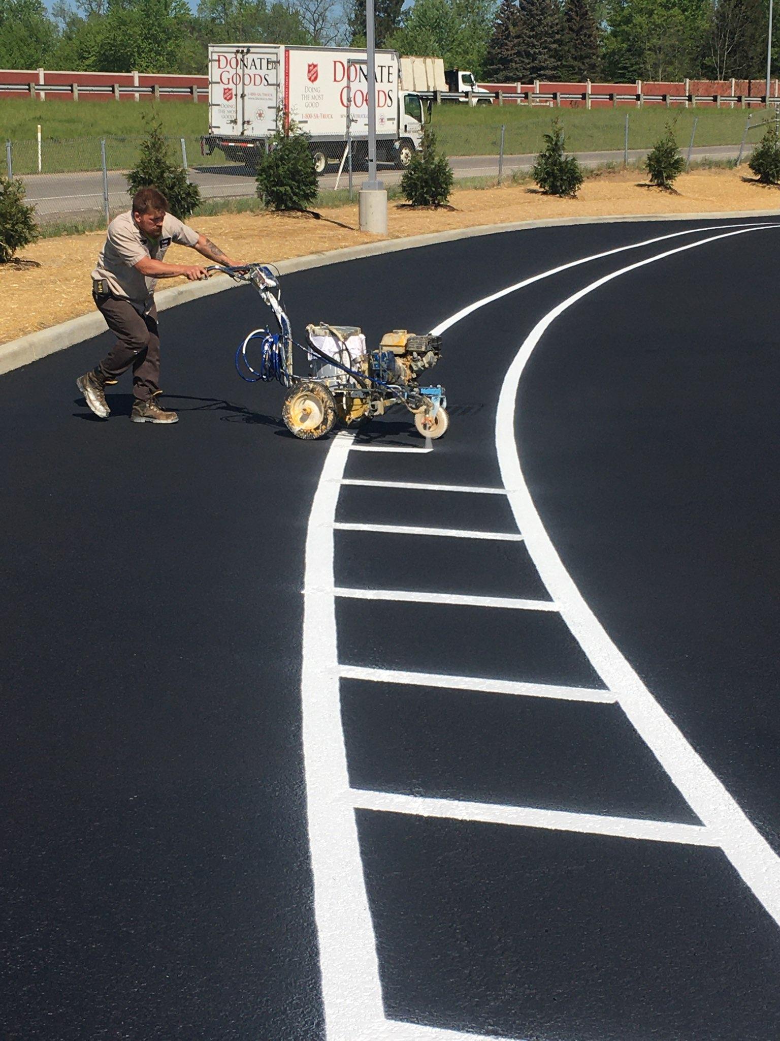 Man using machine to paint white road markings on black asphalt. Outdoors.