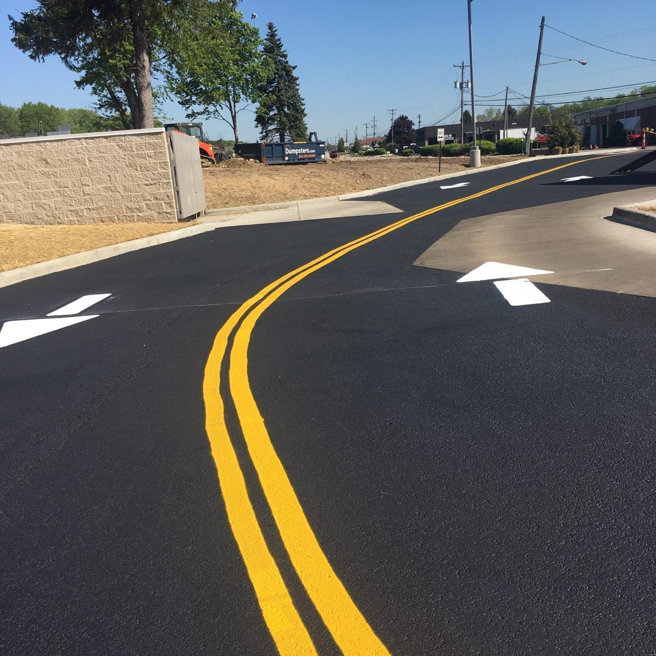 Newly paved road with yellow dividing lines and white directional arrows.