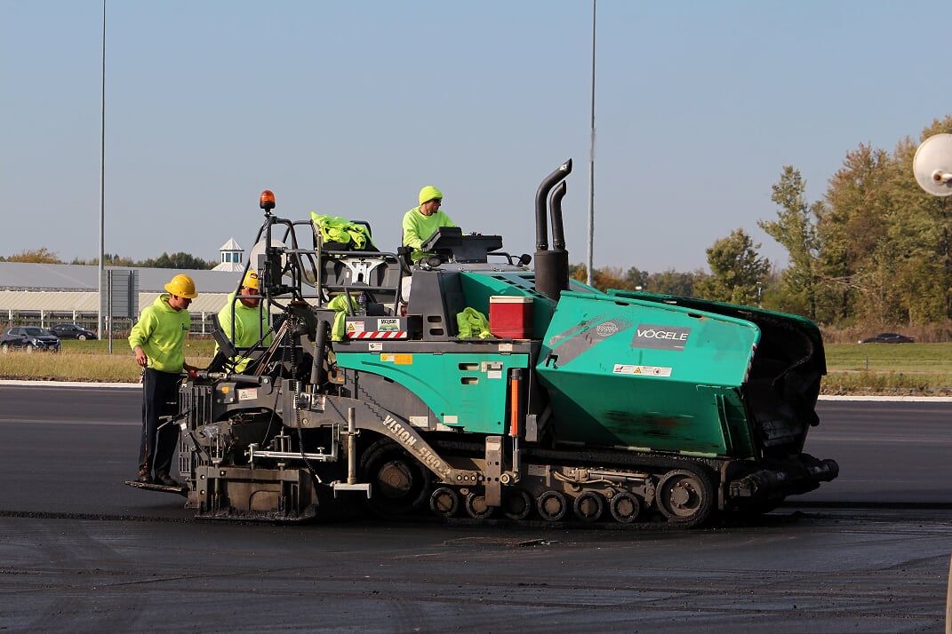 Road paving machine laying asphalt with three workers in safety vests.