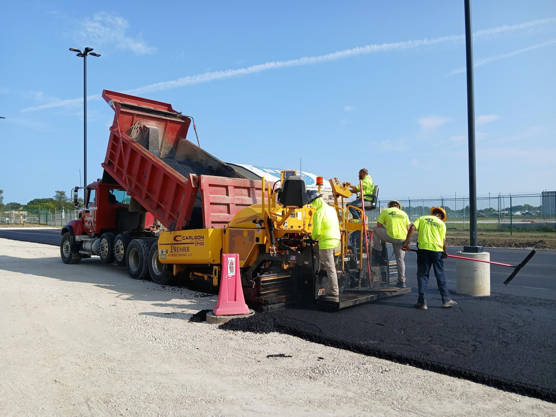 Road paving crew working beside an orange dump truck on a newly laid black asphalt road.