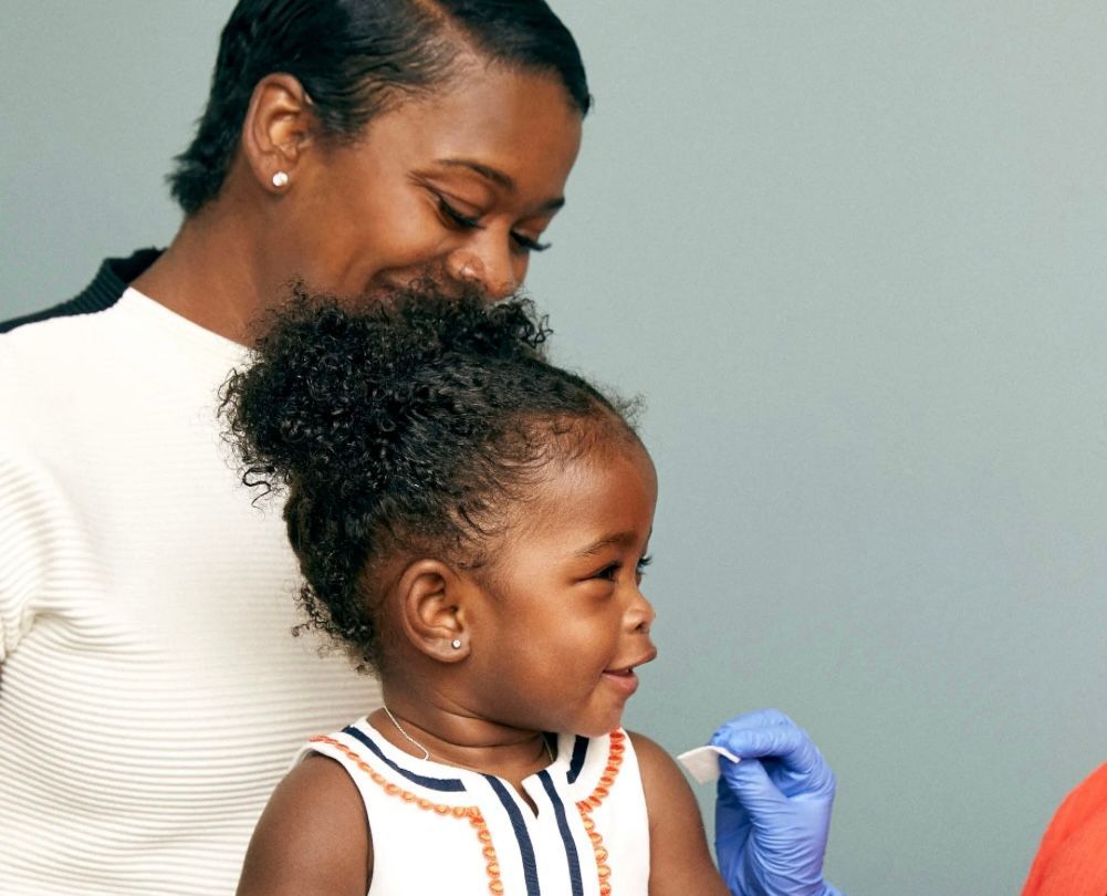 Woman comforts a toddler receiving a shot at a clinic.