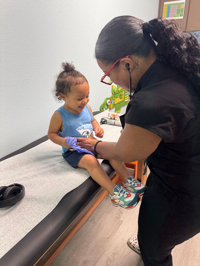 A smiling toddler's leg is examined by a woman with a stethoscope in a medical setting.