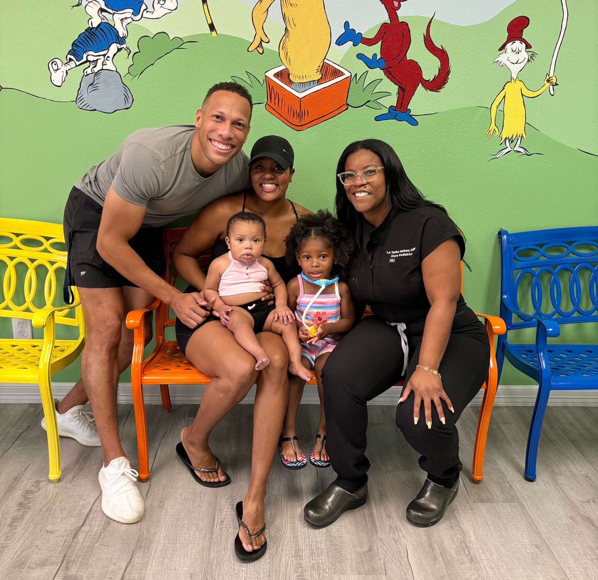 Family seated on colorful benches in a playful mural-decorated room, smiling at the camera.