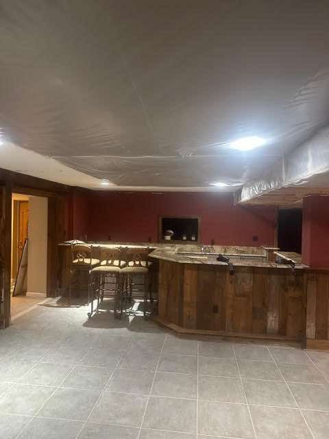 Basement with a rustic wooden bar, stools, and red walls; unfinished ceiling, tiled floor.