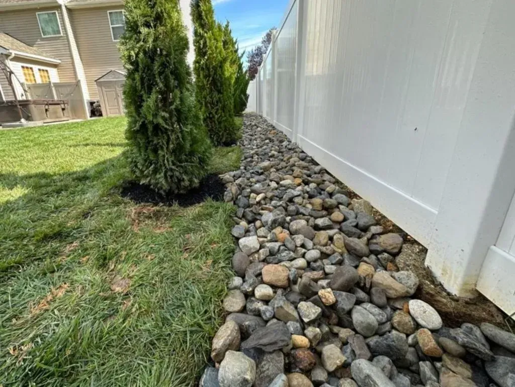 A white fence is surrounded by rocks and grass in a backyard.