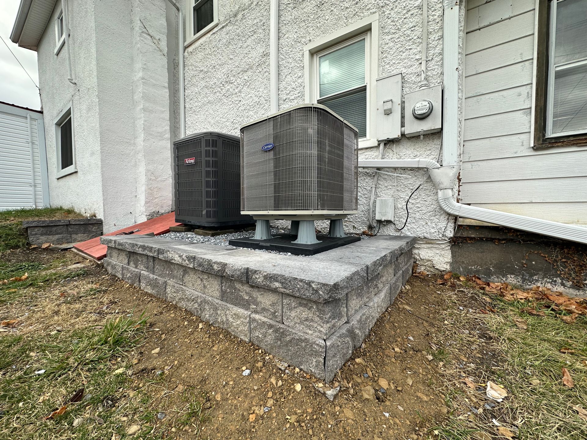 Two air conditioners are sitting on the side of a house.