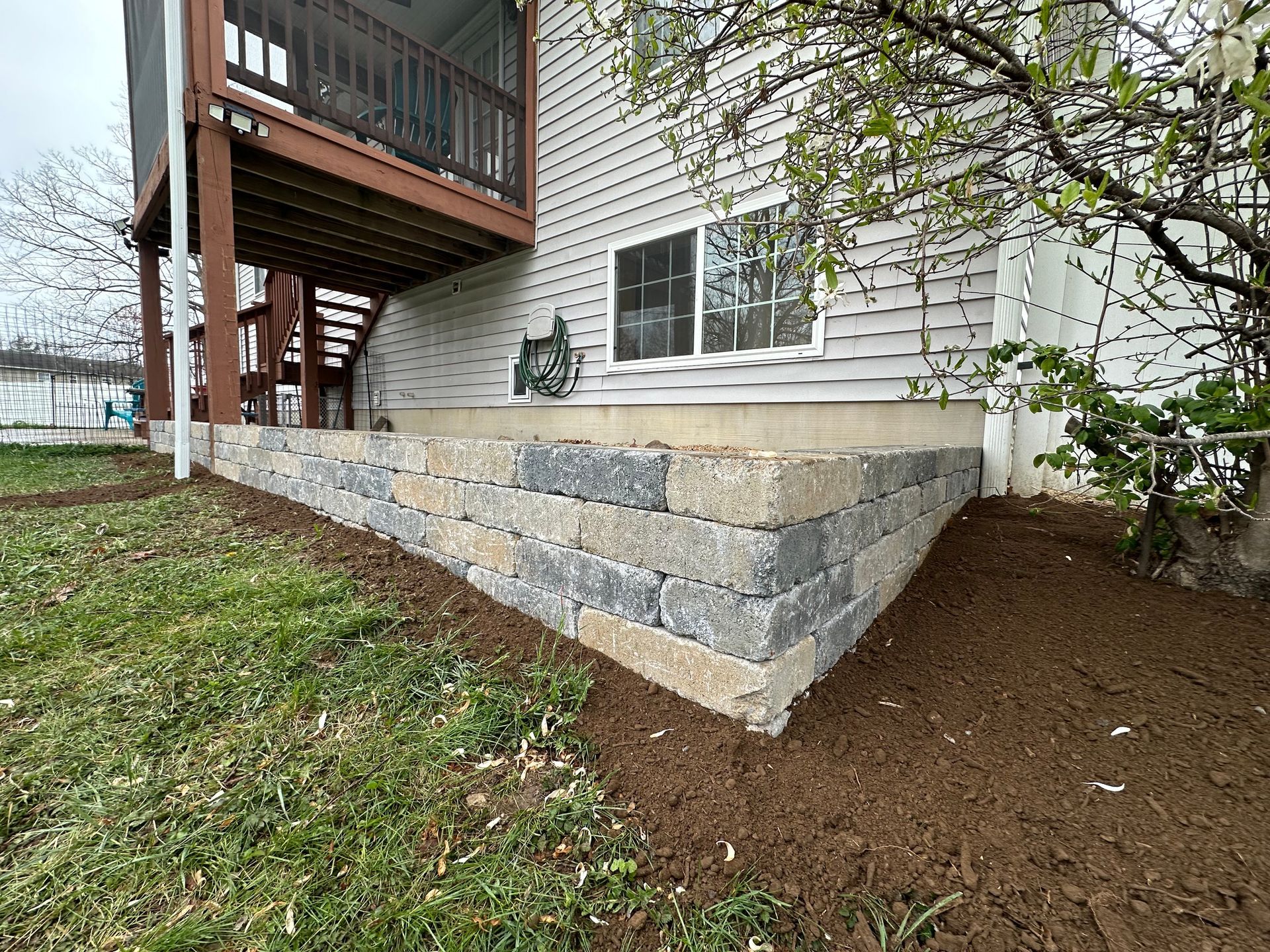 Retaining wall built with gray and tan blocks supporting the foundation of a house.