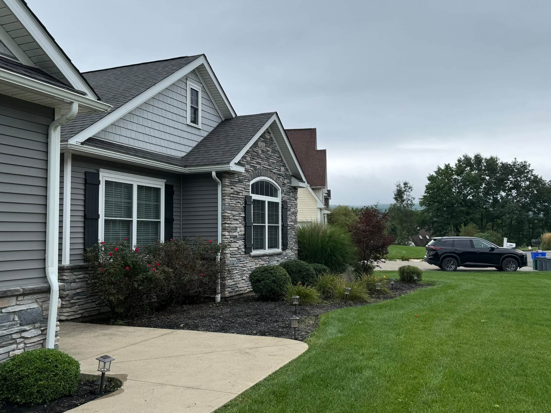 Suburban house with stone facade, green lawn, and a black pickup truck parked outside