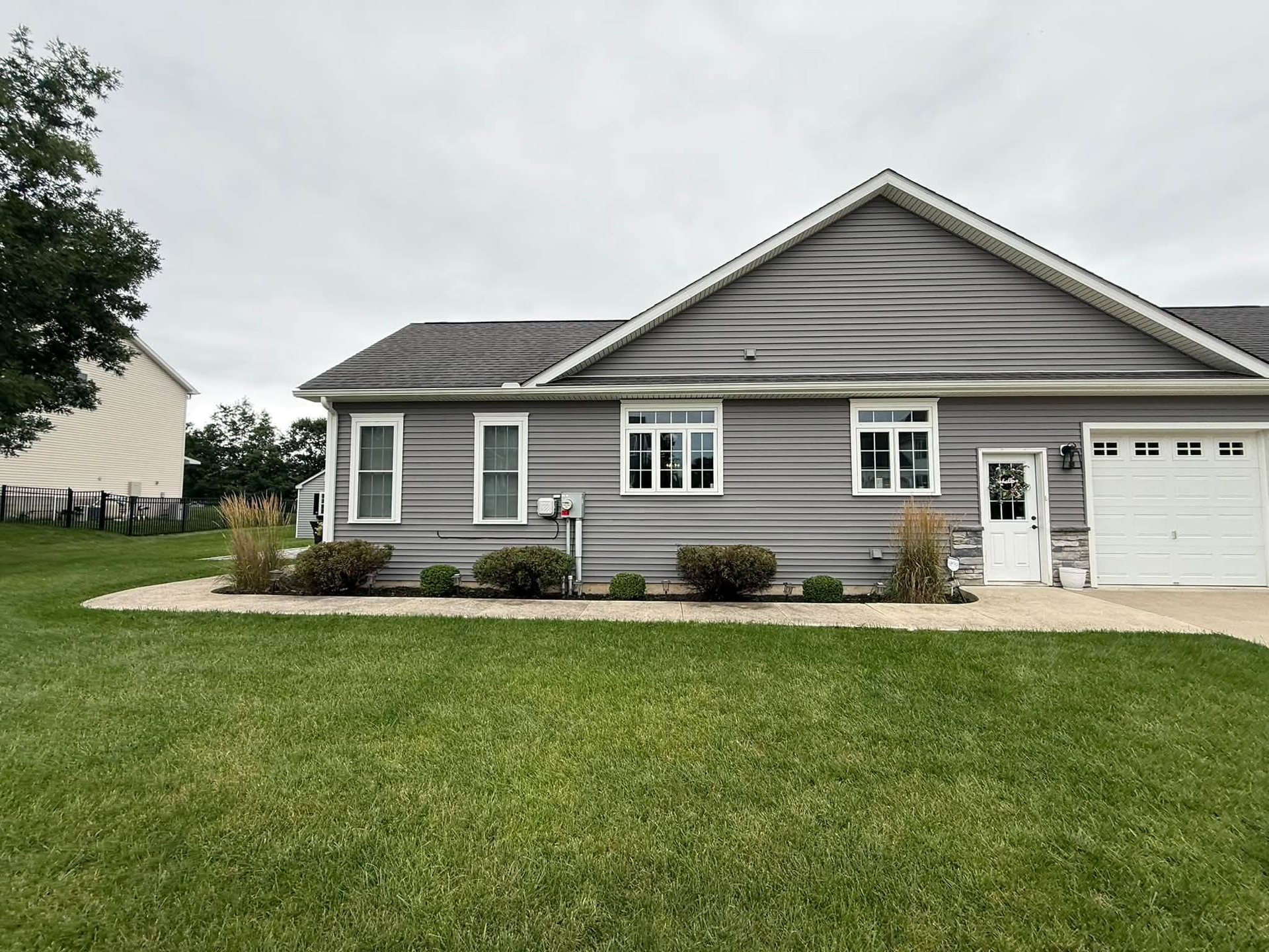 Gray single-story house with white trim and garage, front lawn, and cloudy sky