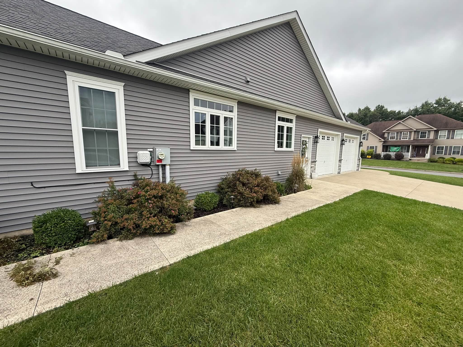 Gray house exterior with white trim, sloped roof, landscaped walkway, and green lawn under cloudy sky