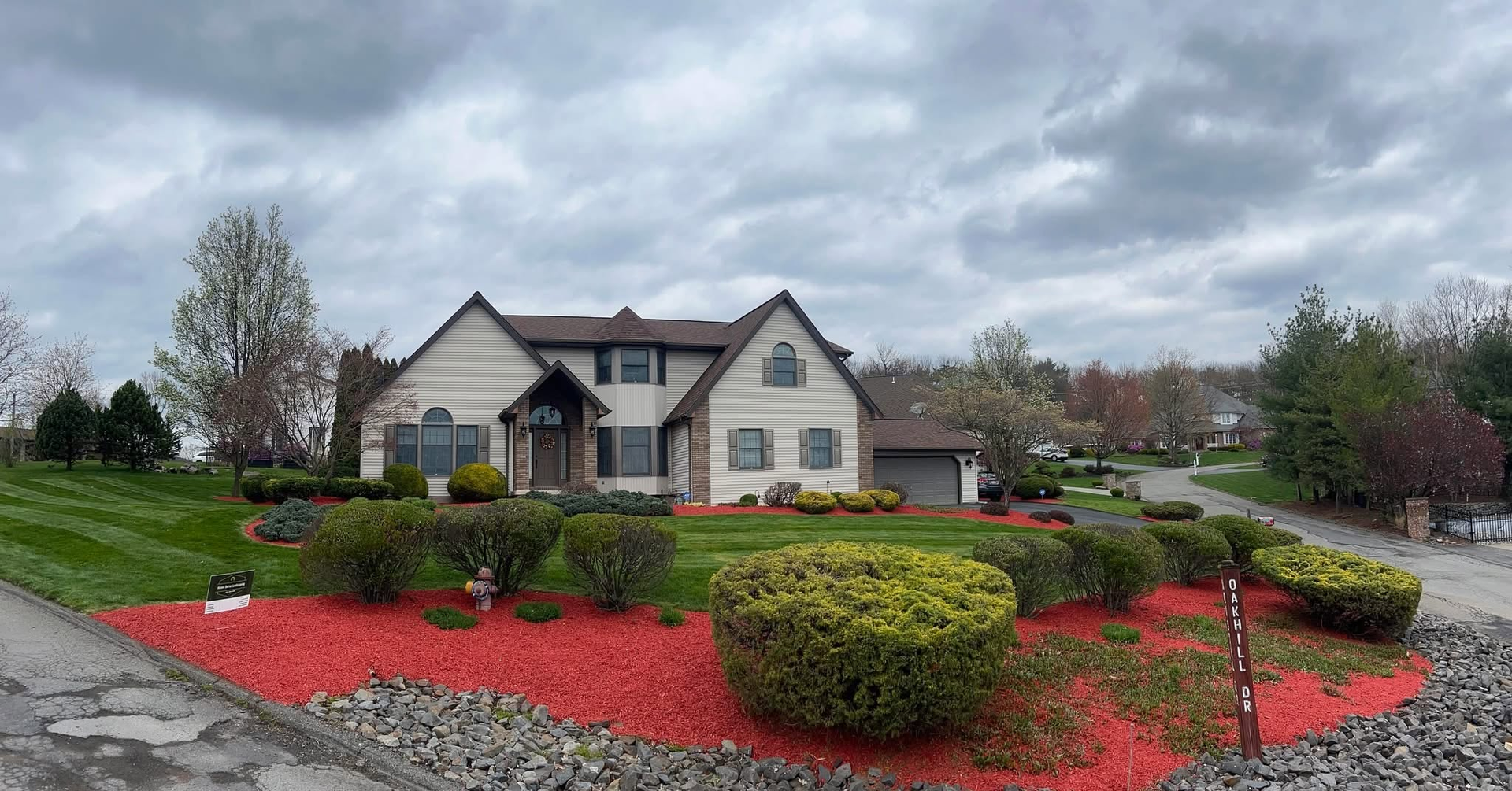 Suburban house with manicured lawn and red mulch under a cloudy sky