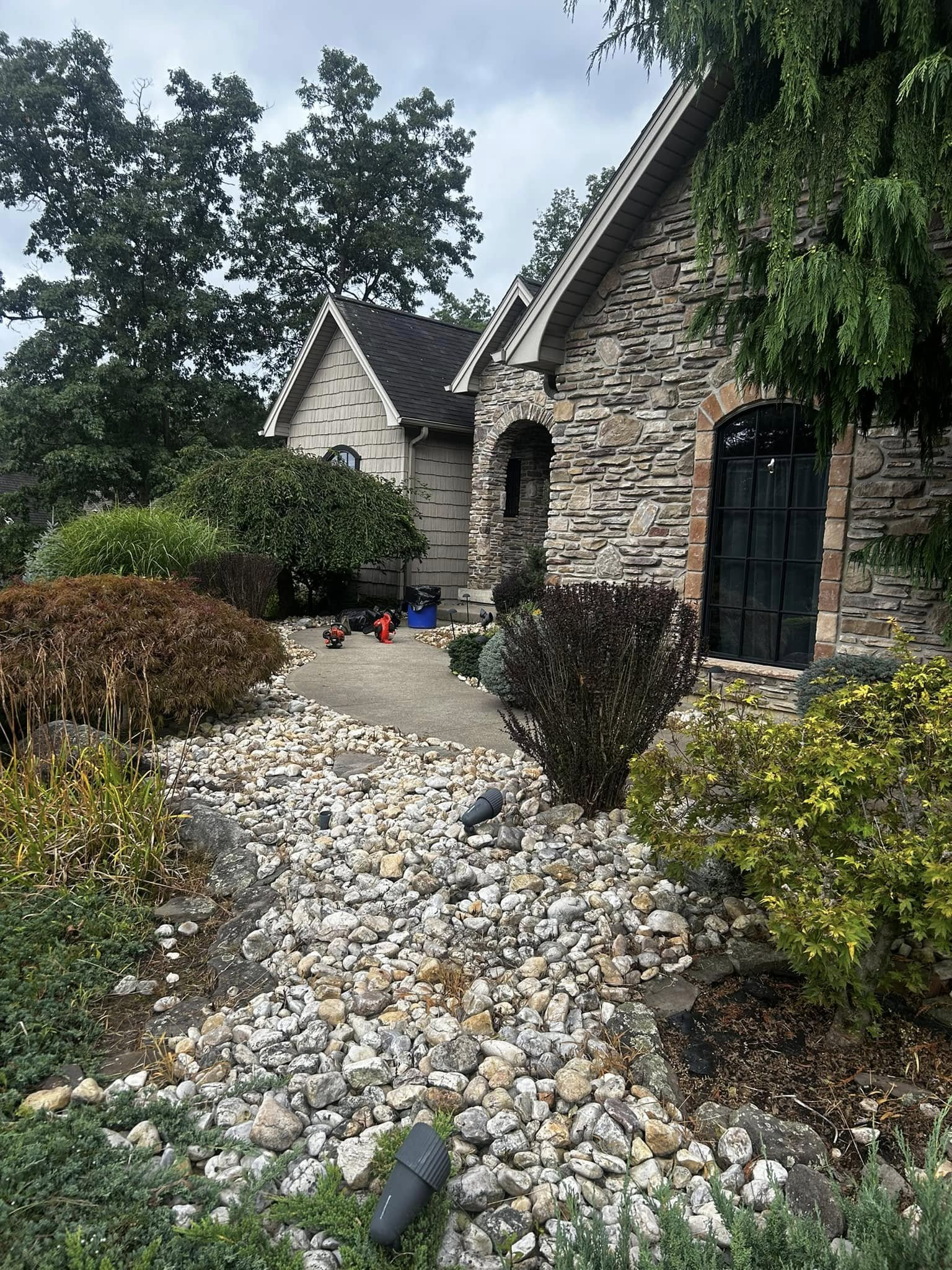 Stone house with a gravel path, shrubs, and trees in a garden setting